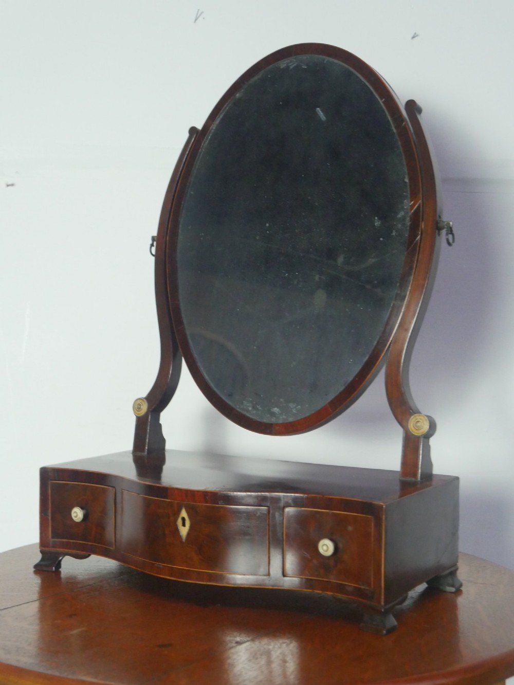 An antique Georgian mahogany dressing mirror with an oval adjustable glass supported on curved arms above a serpentine three-drawer base. View X