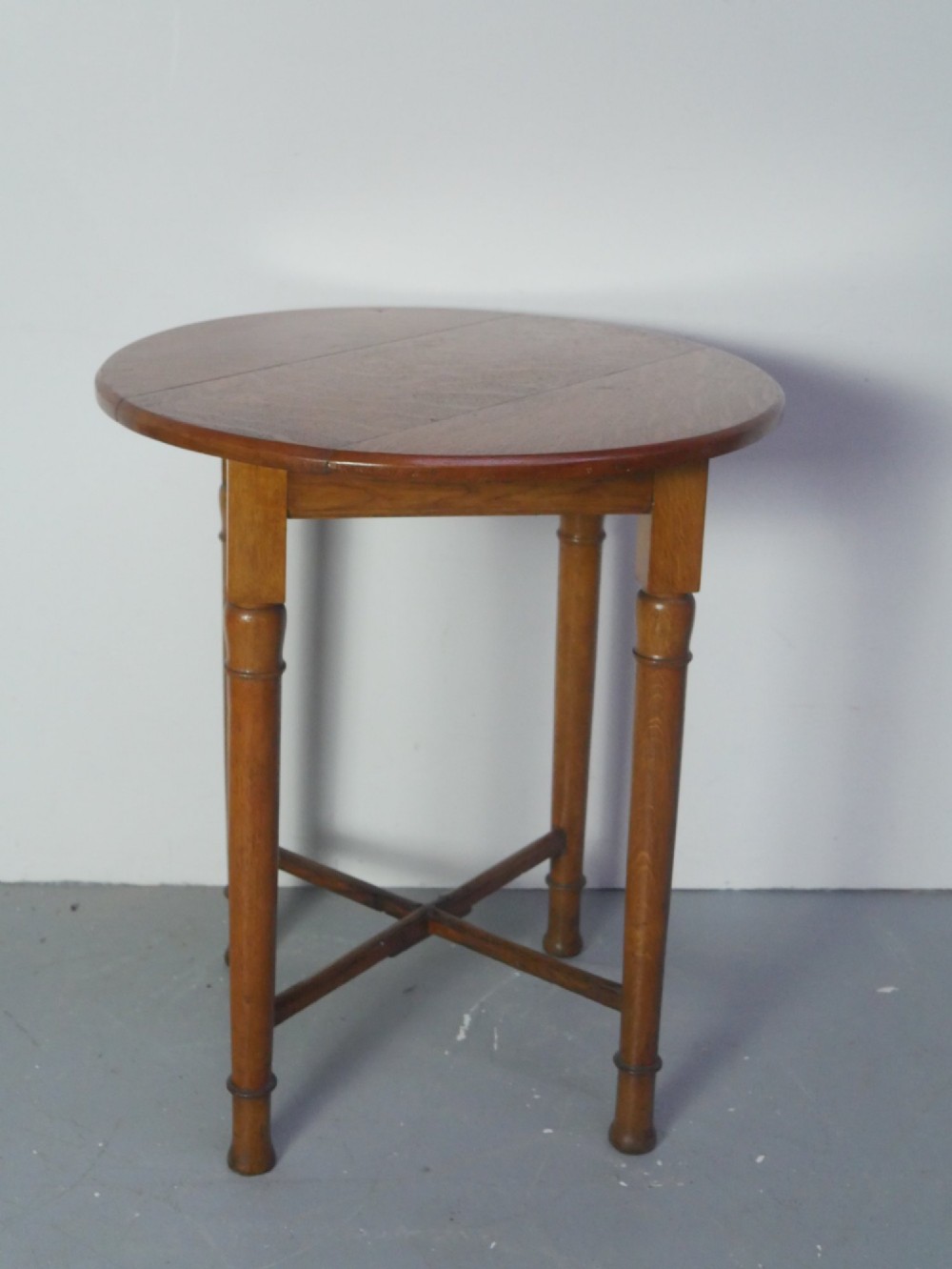 A round 1920s oak lamp table featuring turned legs supported by an X-frame stretcher.