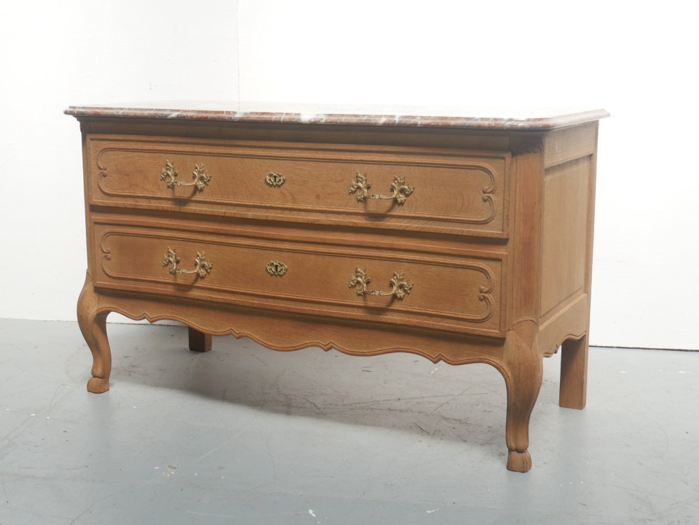 A French provincial style oak chest of drawers featuring two moulded panel drawers, ornate cast brass handles, cabriole legs, and a red-toned marble top.