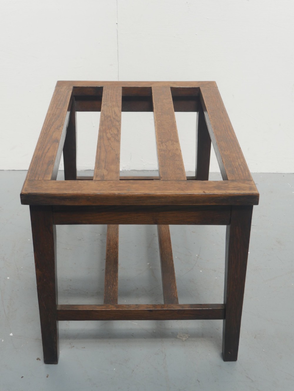 A solid dark oak luggage rack featuring four square legs, supportive stretchers, and a slatted top surface. View II