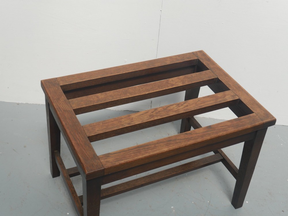A solid dark oak luggage rack featuring four square legs, supportive stretchers, and a slatted top surface. View V
