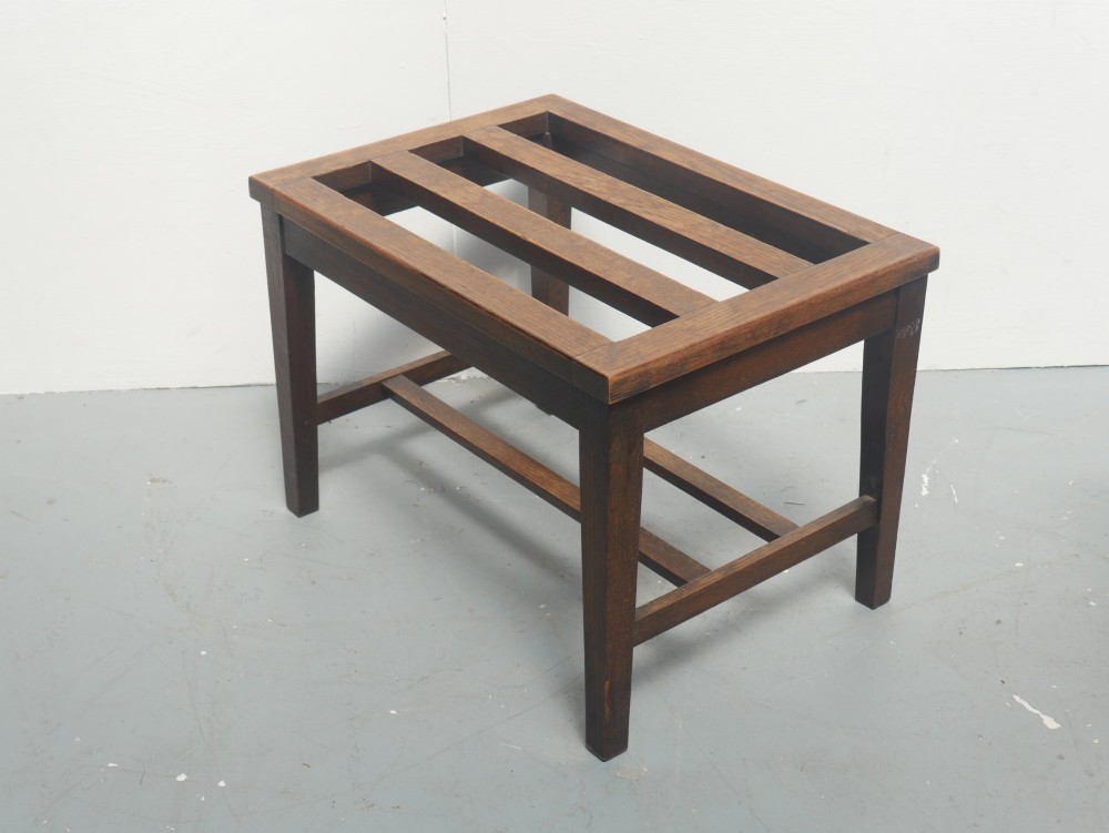 A solid dark oak luggage rack featuring four square legs, supportive stretchers, and a slatted top surface. View VI