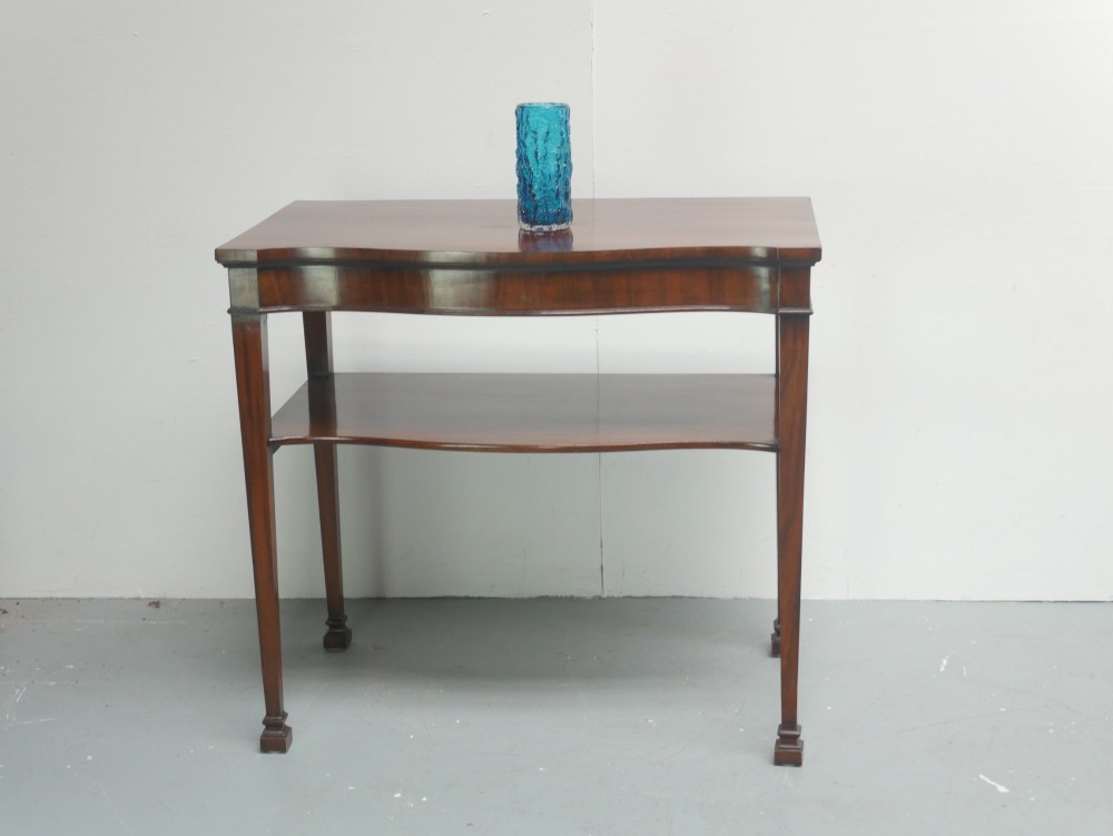 A mahogany console table featuring a shaped top, a lower tier shelf, and tapered square legs.