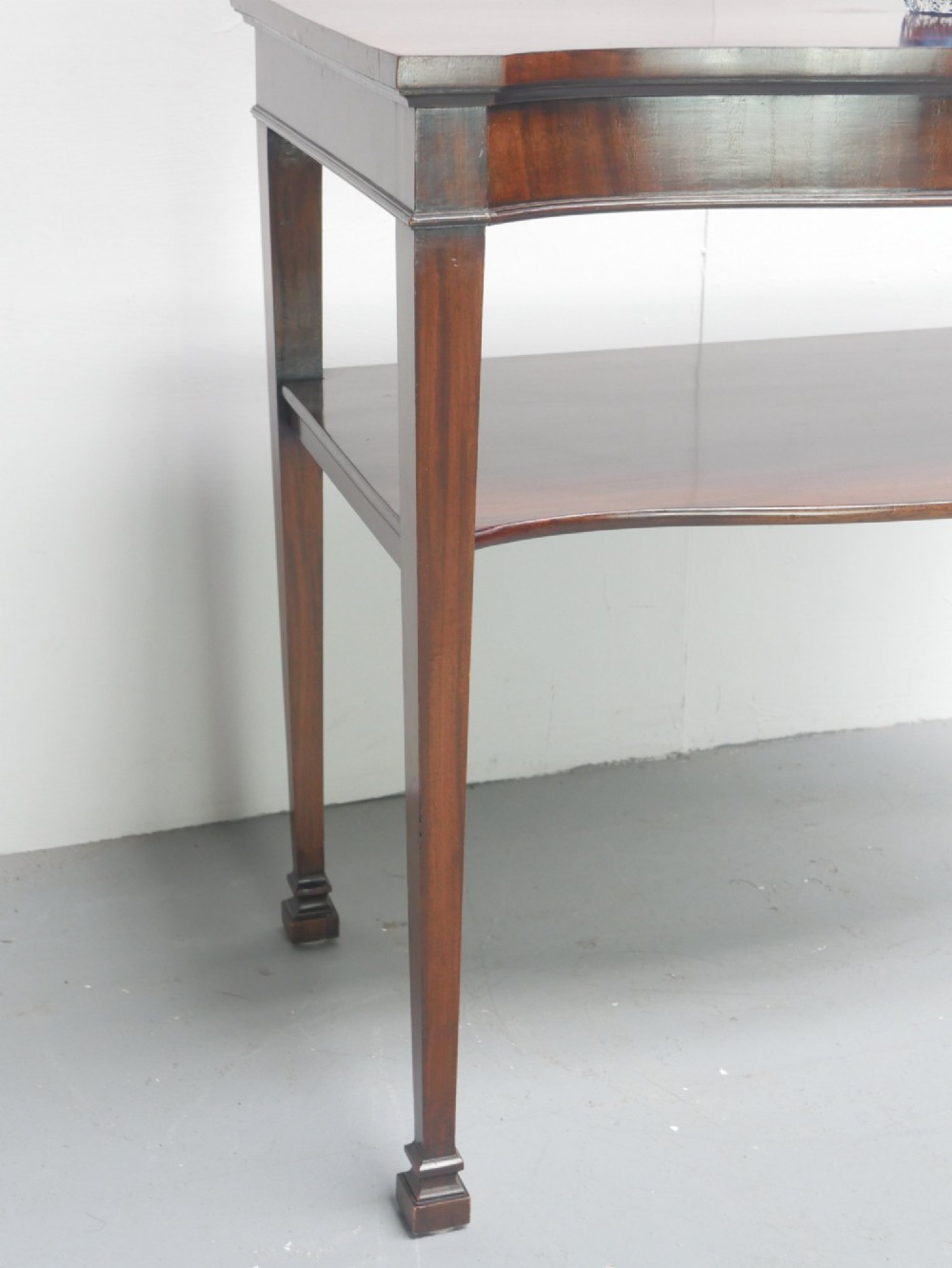 A mahogany console table featuring a shaped top, a lower tier shelf, and tapered square legs. View III