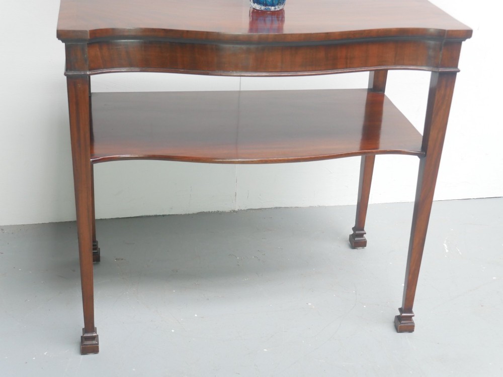 A mahogany console table featuring a shaped top, a lower tier shelf, and tapered square legs. View IV