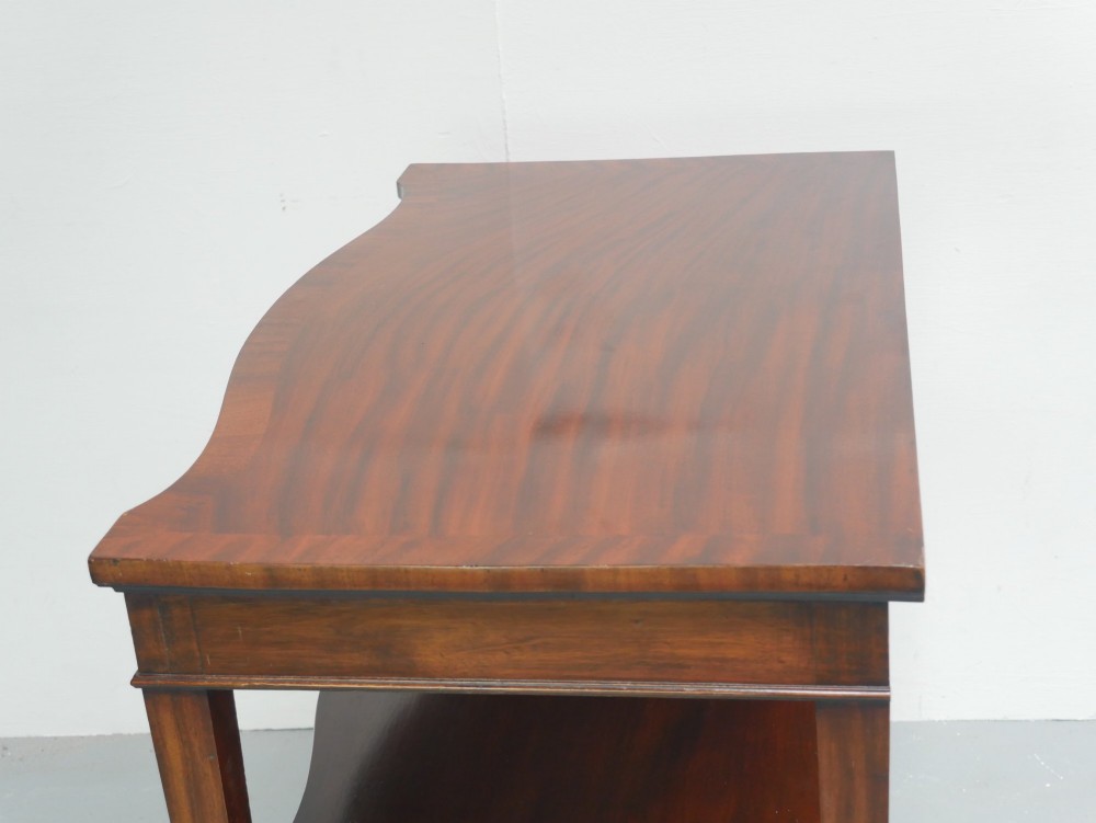 A mahogany console table featuring a shaped top, a lower tier shelf, and tapered square legs. View V