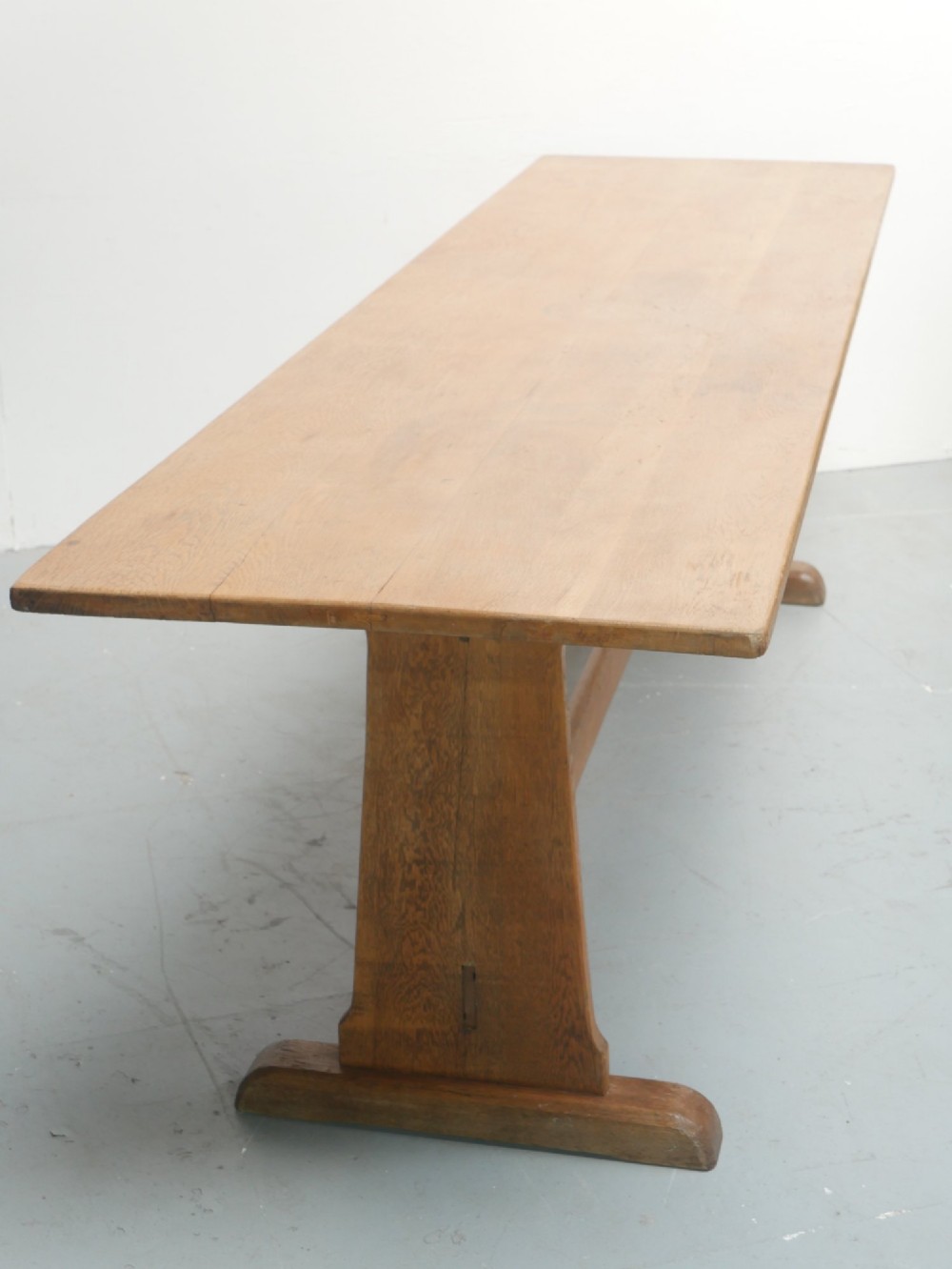 A solid warm brown oak refectory dining table featuring a rectangular plank top, flat trestle leg supports, and a low central stretcher. View II