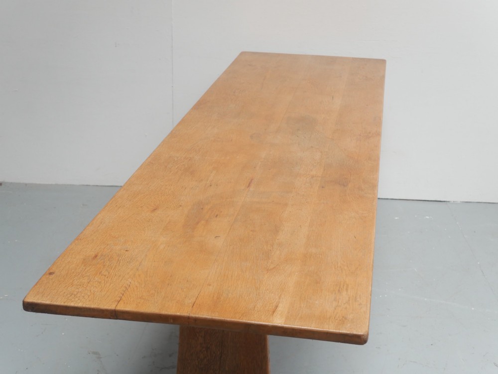 A solid warm brown oak refectory dining table featuring a rectangular plank top, flat trestle leg supports, and a low central stretcher. View III
