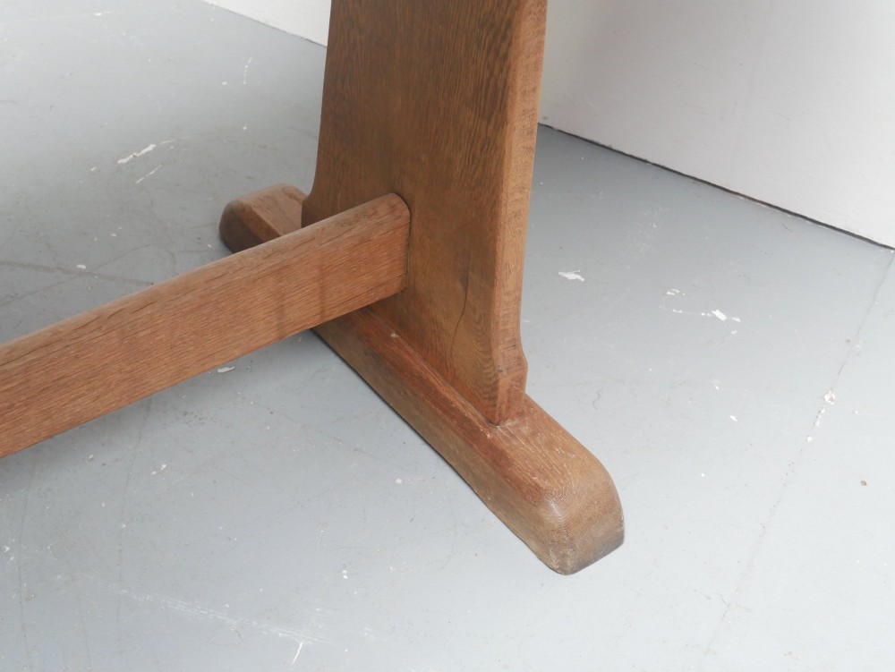 A solid warm brown oak refectory dining table featuring a rectangular plank top, flat trestle leg supports, and a low central stretcher. View IV
