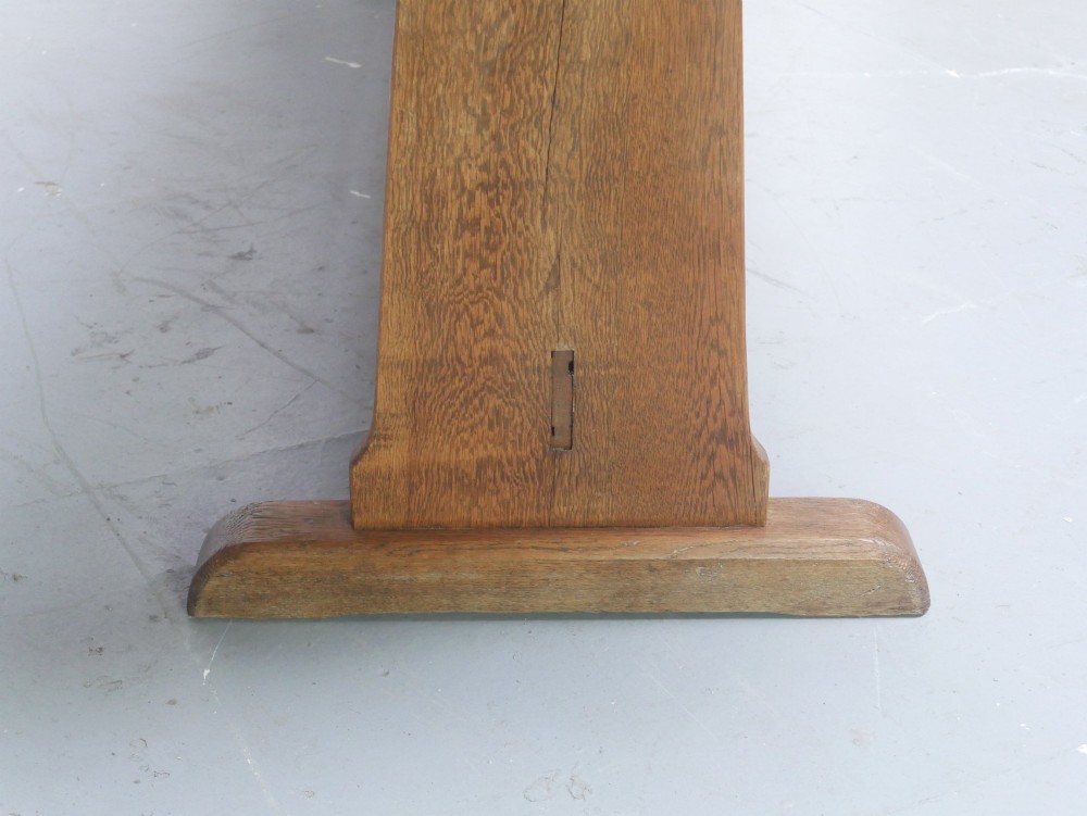 A solid warm brown oak refectory dining table featuring a rectangular plank top, flat trestle leg supports, and a low central stretcher. View V