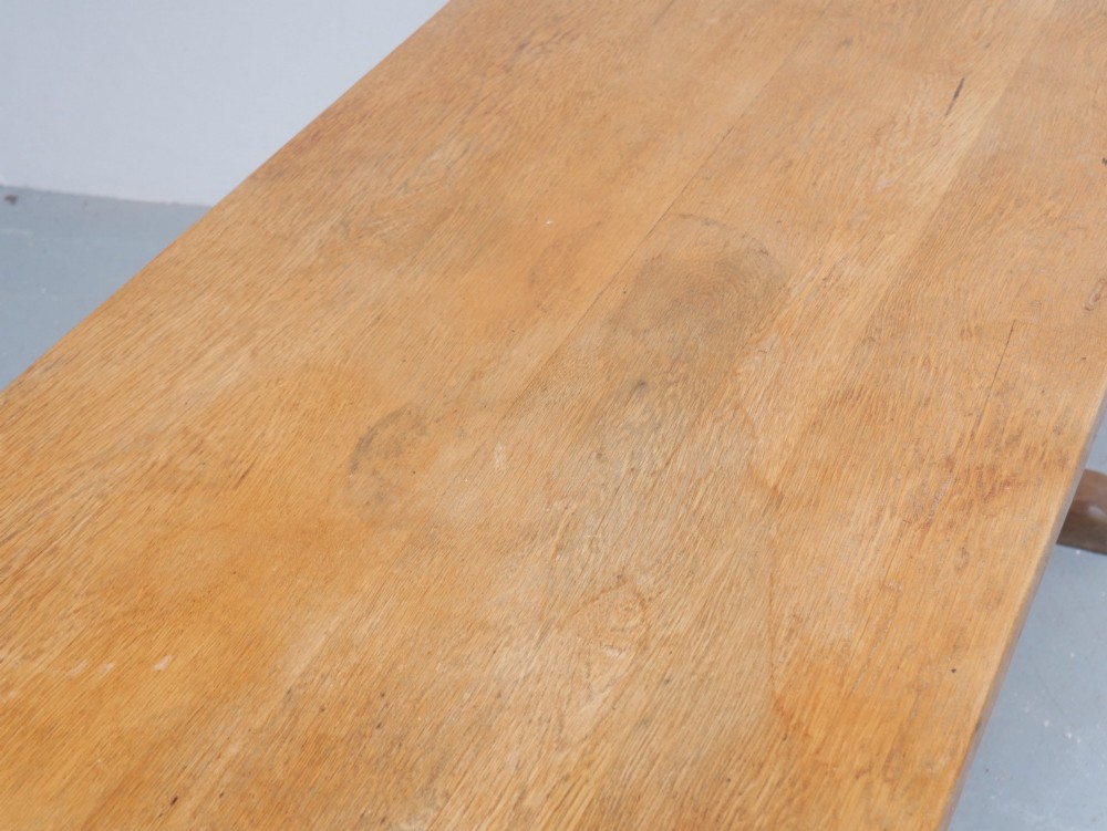 A solid warm brown oak refectory dining table featuring a rectangular plank top, flat trestle leg supports, and a low central stretcher. View VII