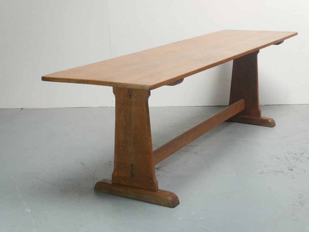 A solid warm brown oak refectory dining table featuring a rectangular plank top, flat trestle leg supports, and a low central stretcher. View IX