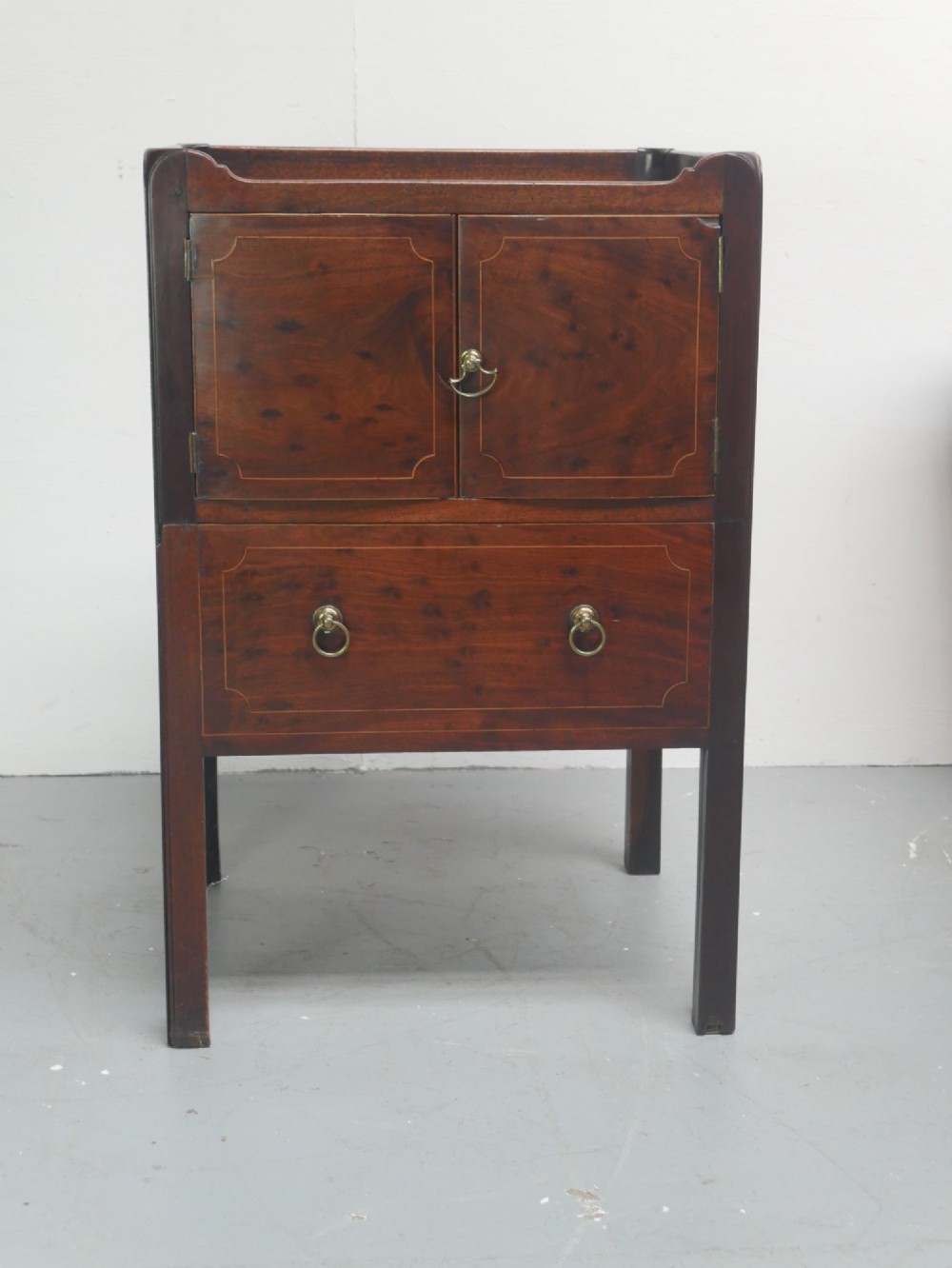 A Georgian mahogany bedside cabinet with a tray top gallery, double inlaid cupboard doors, a lower drawer, and square legs.