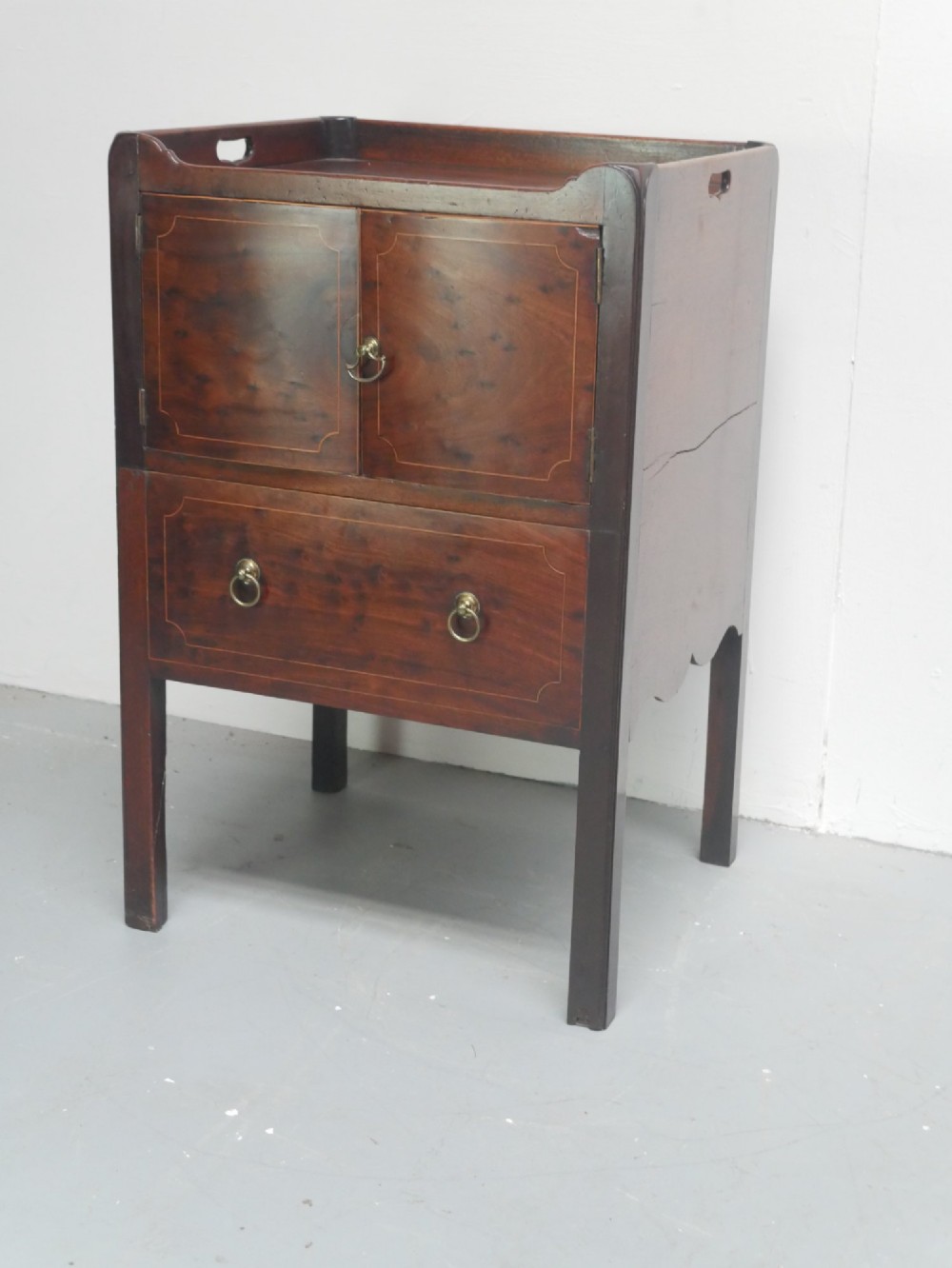 A Georgian mahogany bedside cabinet with a tray top gallery, double inlaid cupboard doors, a lower drawer, and square legs. View II