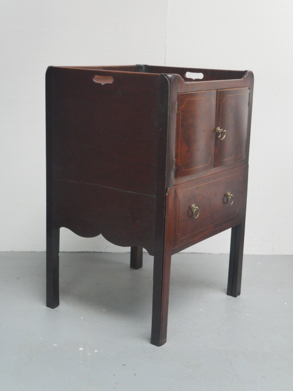 A Georgian mahogany bedside cabinet with a tray top gallery, double inlaid cupboard doors, a lower drawer, and square legs. View IV