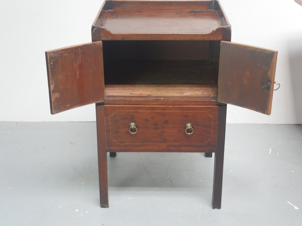 A Georgian mahogany bedside cabinet with a tray top gallery, double inlaid cupboard doors, a lower drawer, and square legs. View VI