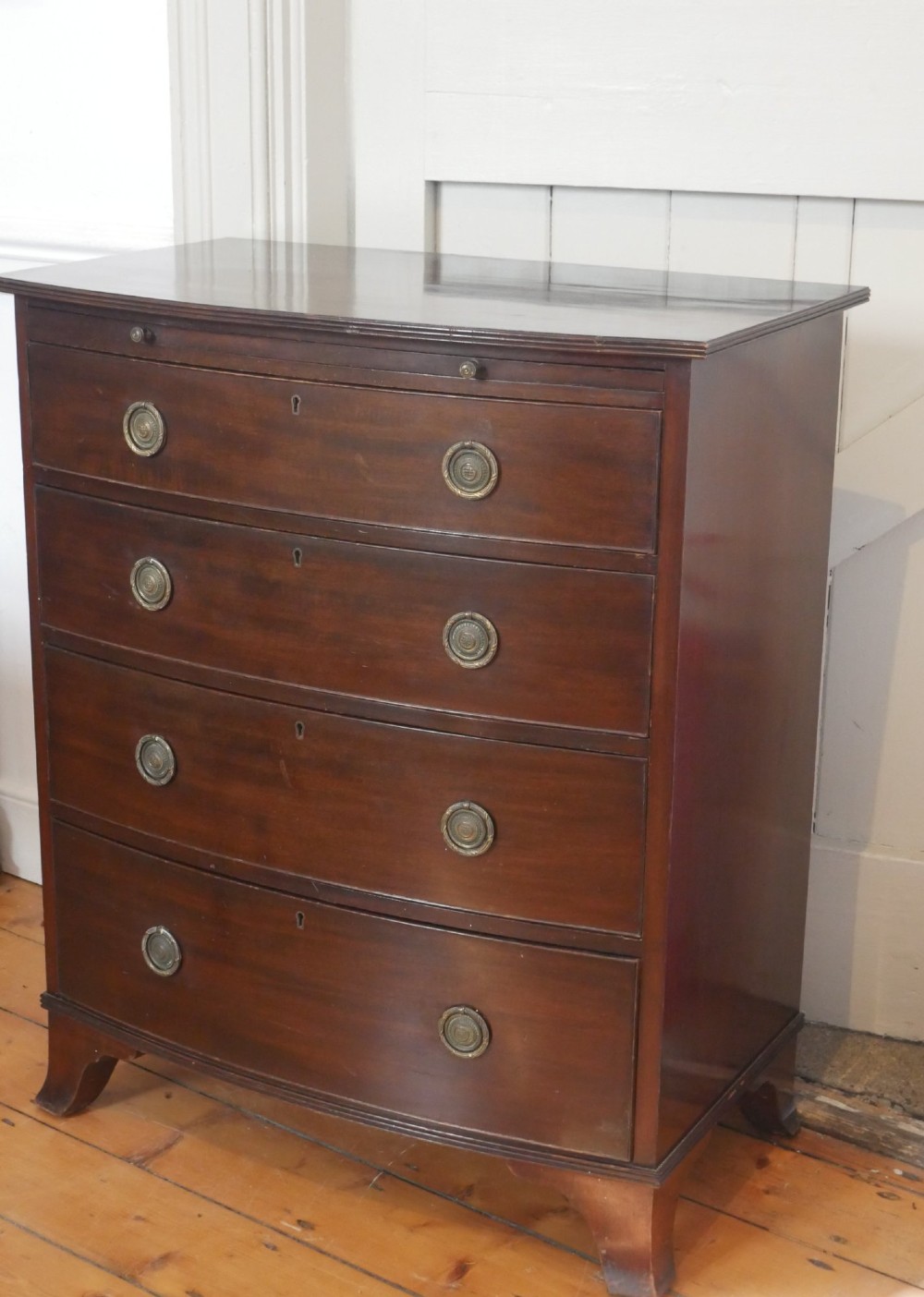 An antique dark mahogany bowfront chest of drawers featuring four graduated drawers with brass ring handles and splayed bracket feet. View II