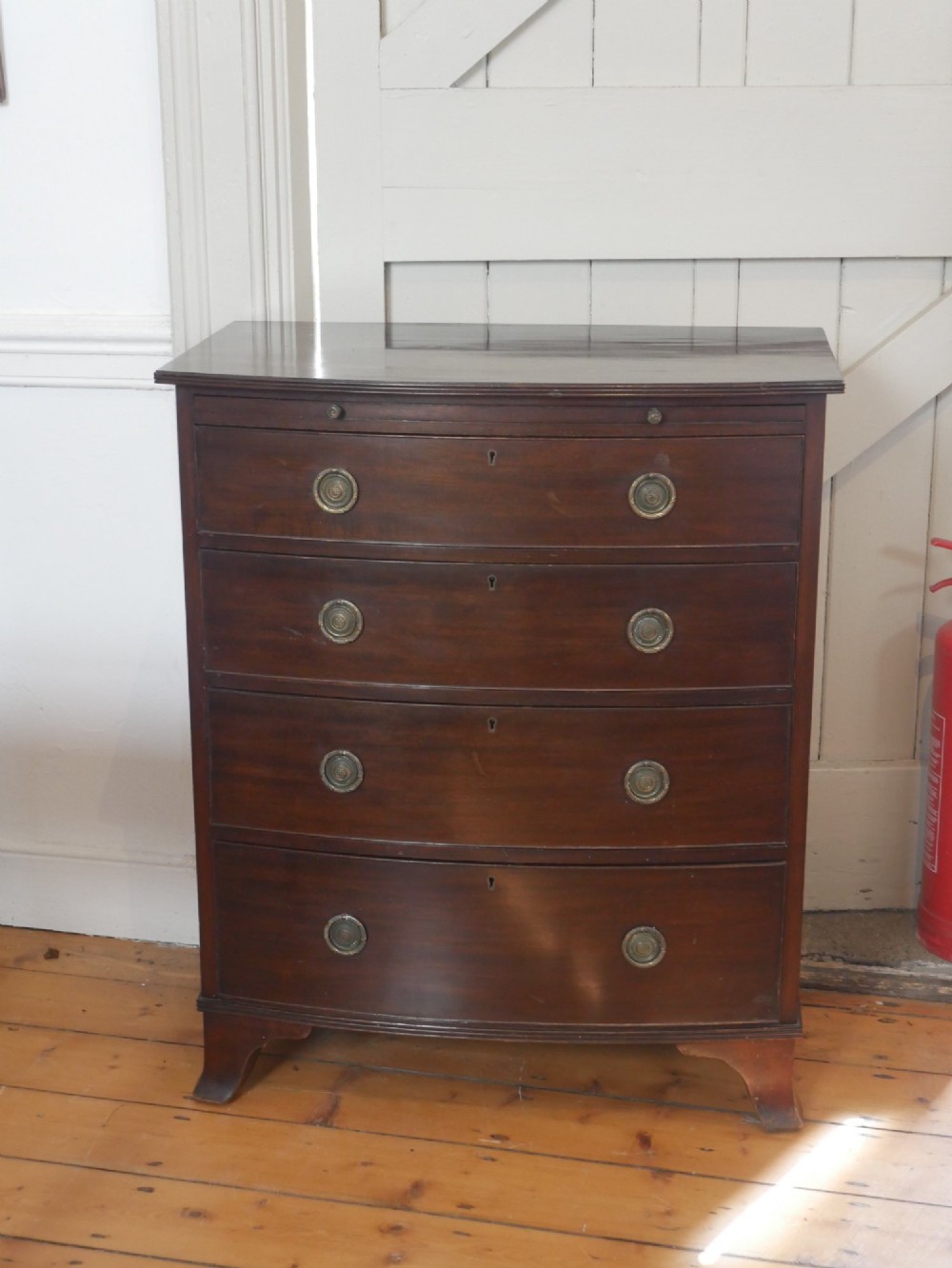 An antique dark mahogany bowfront chest of drawers featuring four graduated drawers with brass ring handles and splayed bracket feet. View III