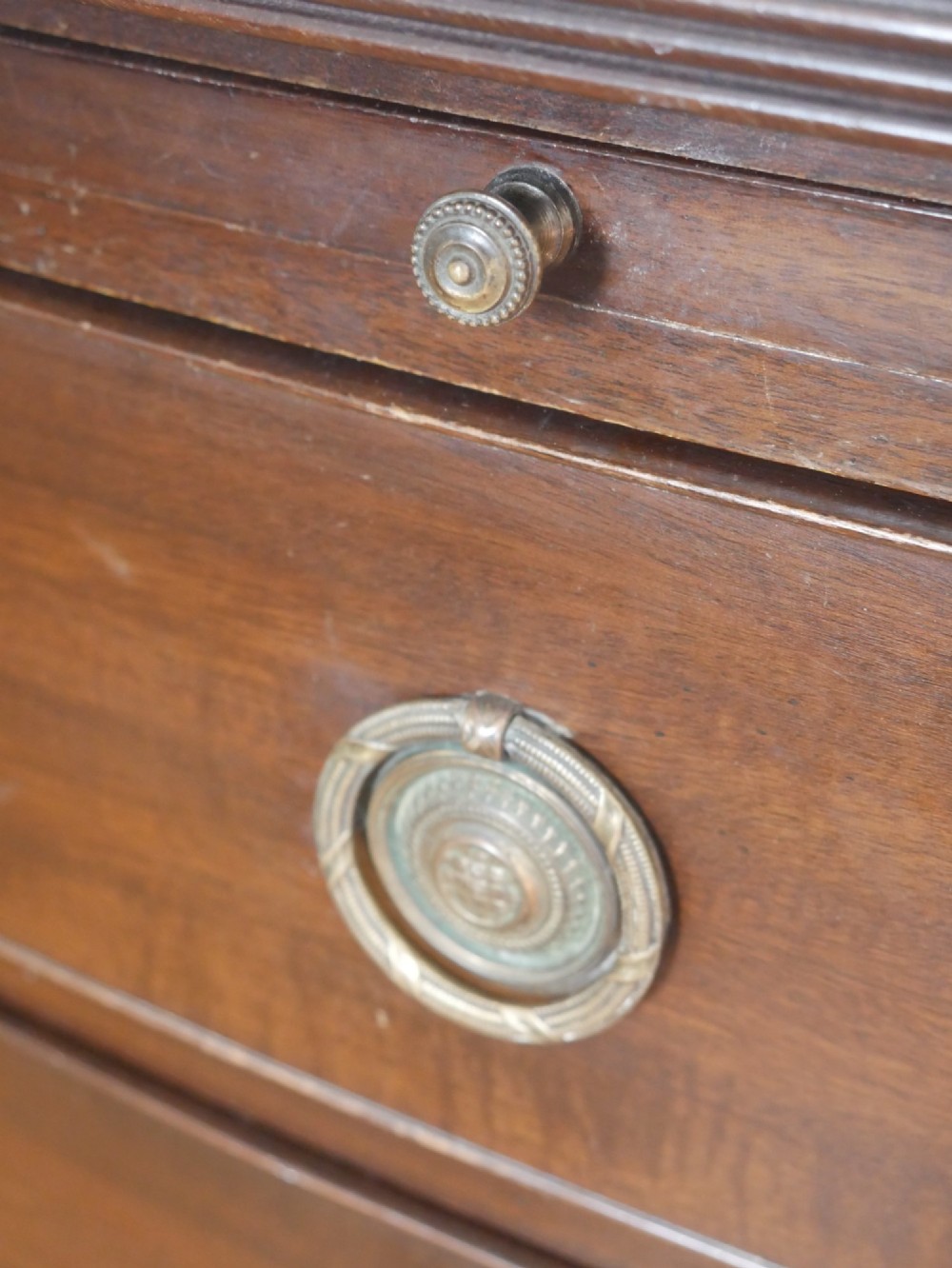 An antique dark mahogany bowfront chest of drawers featuring four graduated drawers with brass ring handles and splayed bracket feet. View IV