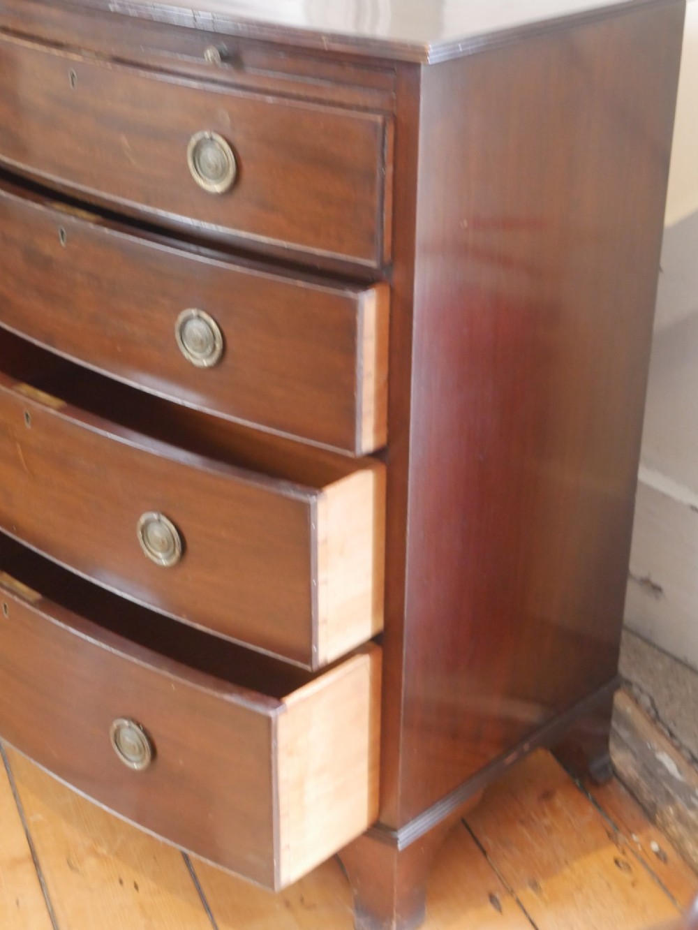An antique dark mahogany bowfront chest of drawers featuring four graduated drawers with brass ring handles and splayed bracket feet. View VI