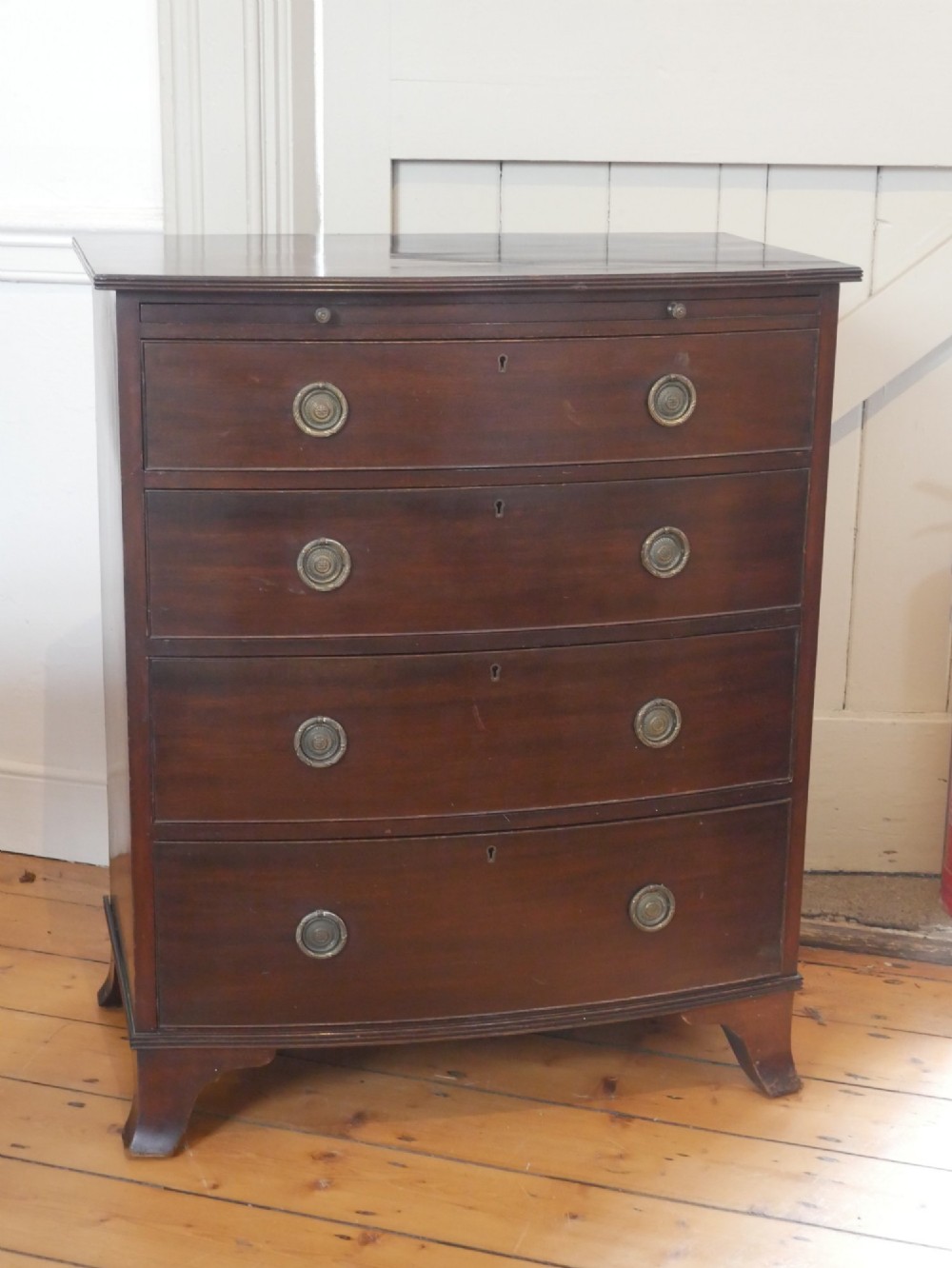 An antique dark mahogany bowfront chest of drawers featuring four graduated drawers with brass ring handles and splayed bracket feet. View IX