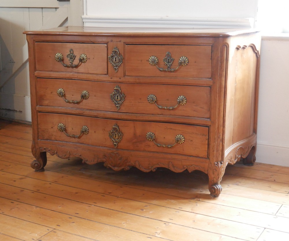 An eighteenth-century French provincial walnut commode featuring three drawers with brass handles, a carved apron, and short cabriole legs.