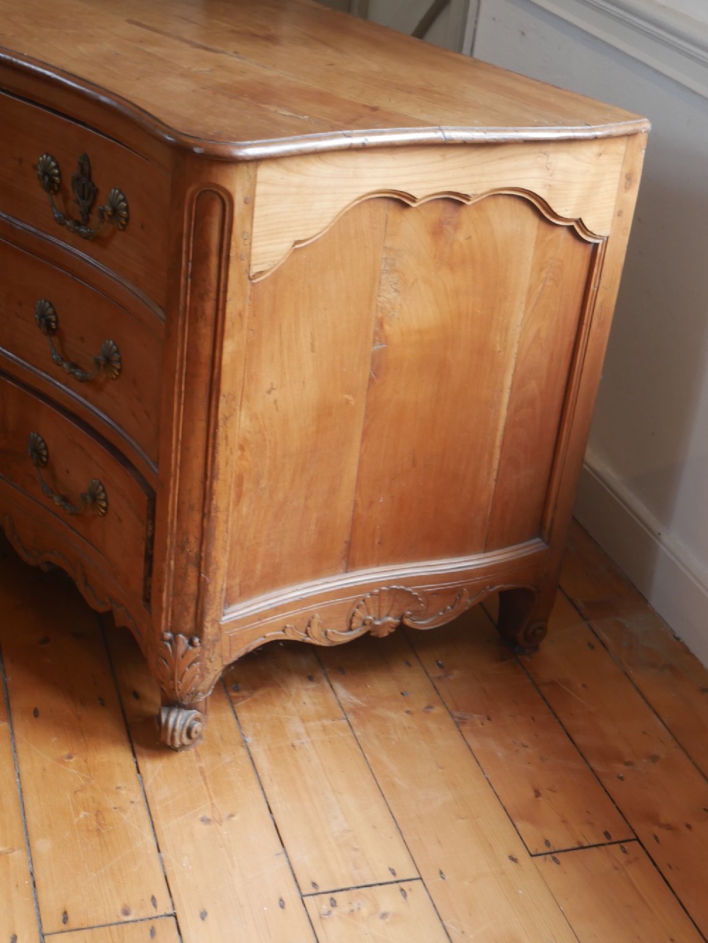 An eighteenth-century French provincial walnut commode featuring three drawers with brass handles, a carved apron, and short cabriole legs. View V