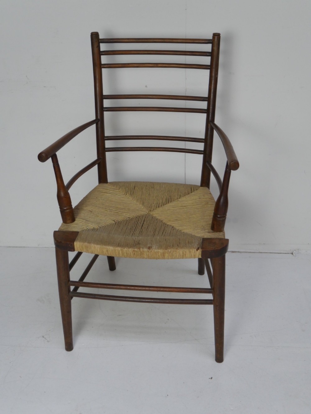 An Arts and Crafts style dark wood armchair featuring a multi-slat ladder back, slender curved armrests, and a hand-woven natural rush seat. View II