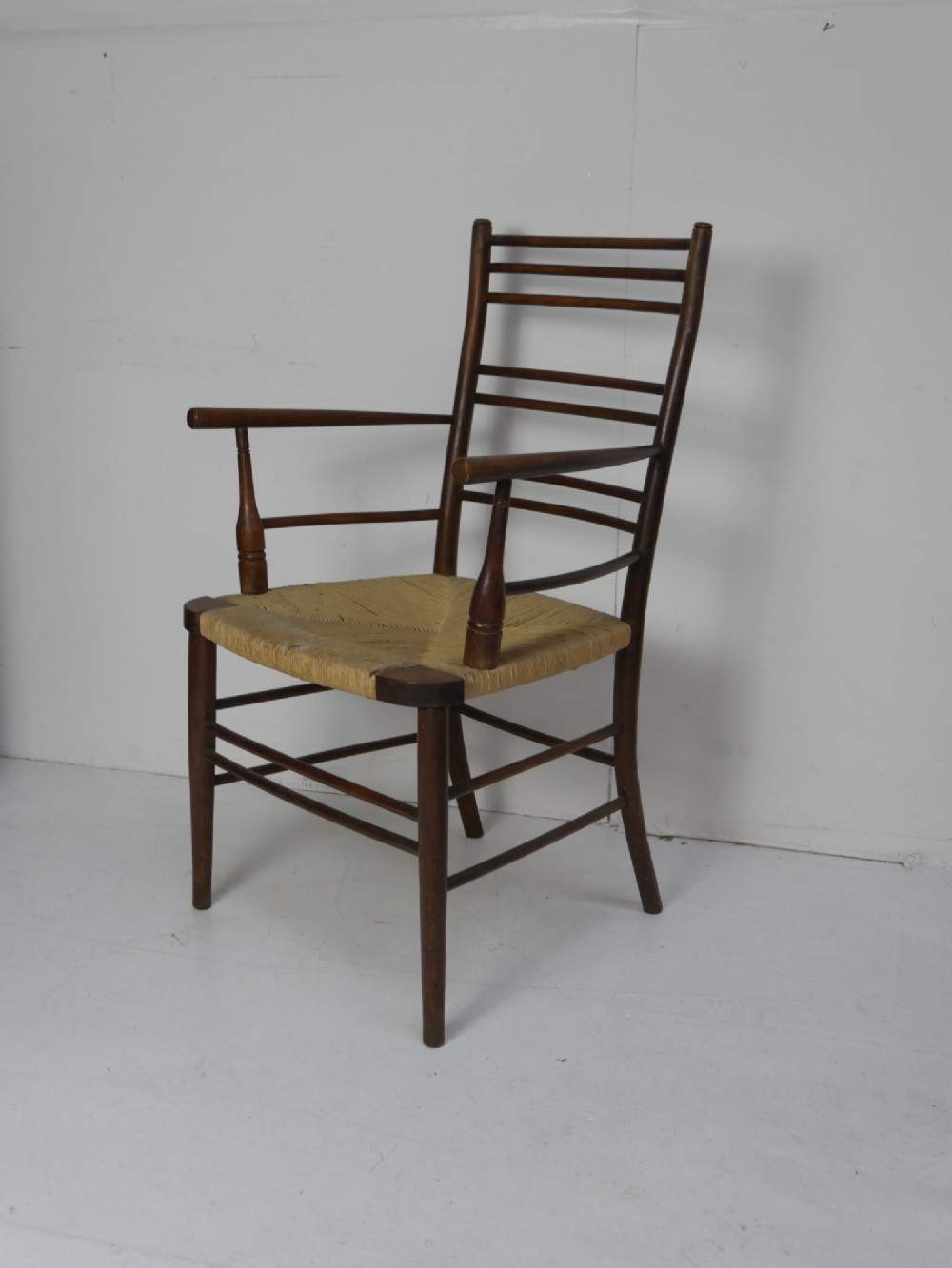 An Arts and Crafts style dark wood armchair featuring a multi-slat ladder back, slender curved armrests, and a hand-woven natural rush seat. View III