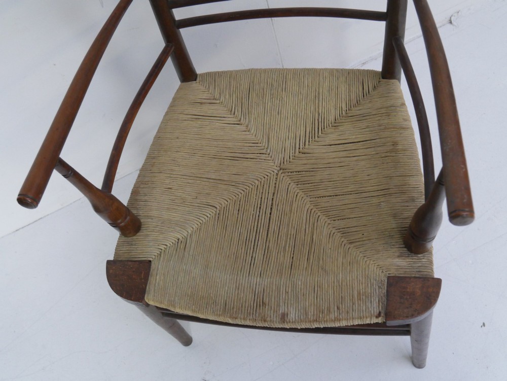 An Arts and Crafts style dark wood armchair featuring a multi-slat ladder back, slender curved armrests, and a hand-woven natural rush seat. View IV
