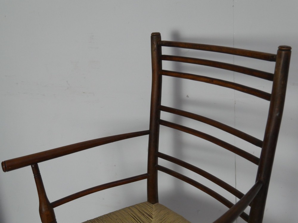An Arts and Crafts style dark wood armchair featuring a multi-slat ladder back, slender curved armrests, and a hand-woven natural rush seat. View V