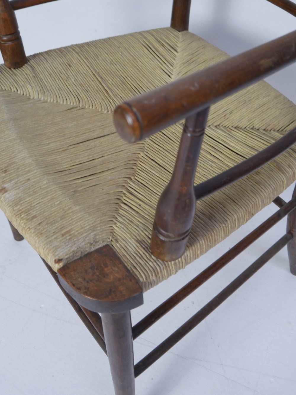 An Arts and Crafts style dark wood armchair featuring a multi-slat ladder back, slender curved armrests, and a hand-woven natural rush seat. View VI