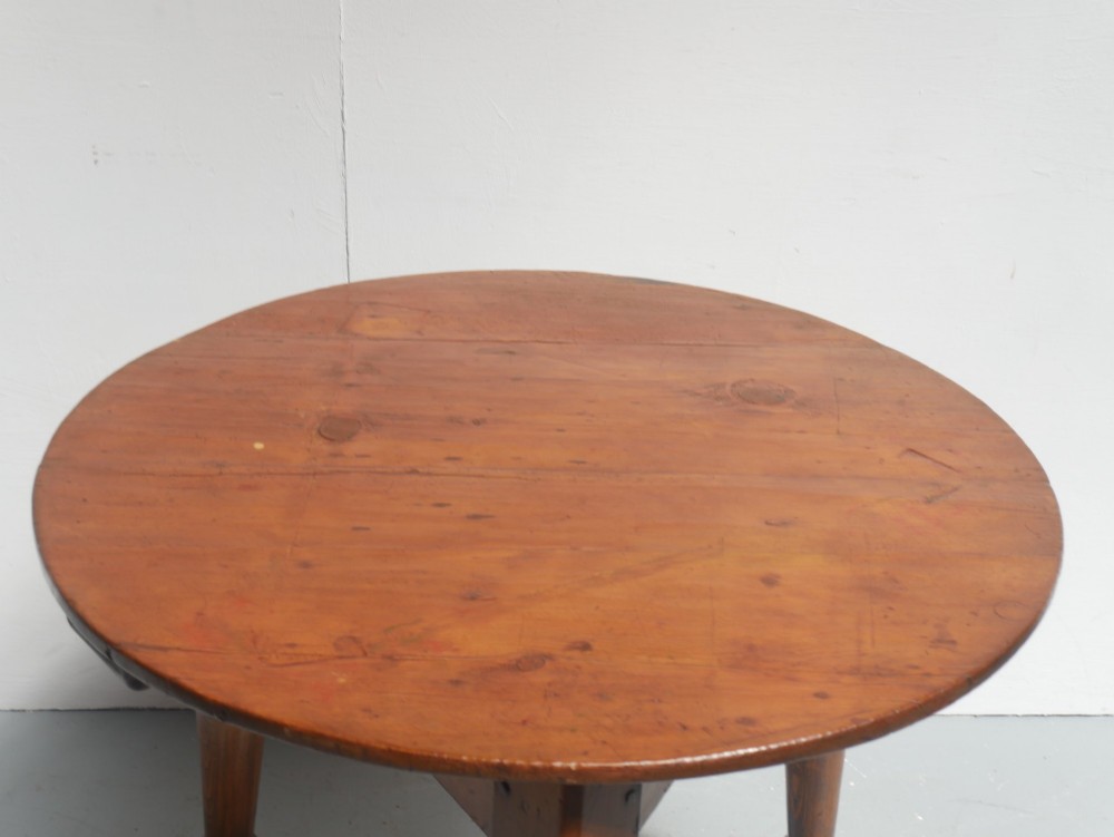 A circular pine cricket table featuring three turned legs joined by a deep triangular apron in a warm brown timber finish. View II