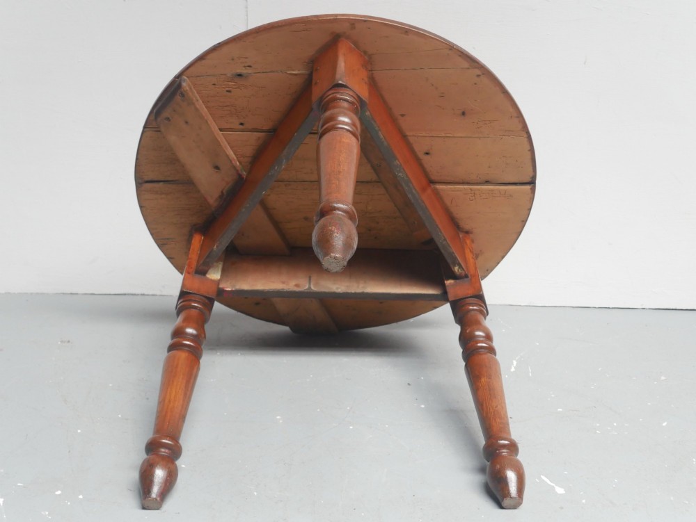 A circular pine cricket table featuring three turned legs joined by a deep triangular apron in a warm brown timber finish. View III