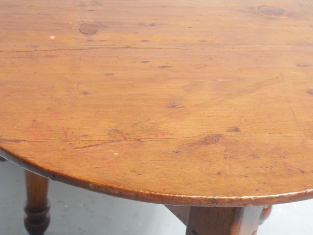 A circular pine cricket table featuring three turned legs joined by a deep triangular apron in a warm brown timber finish. View V