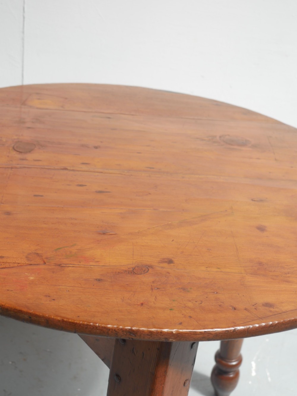 A circular pine cricket table featuring three turned legs joined by a deep triangular apron in a warm brown timber finish. View VI