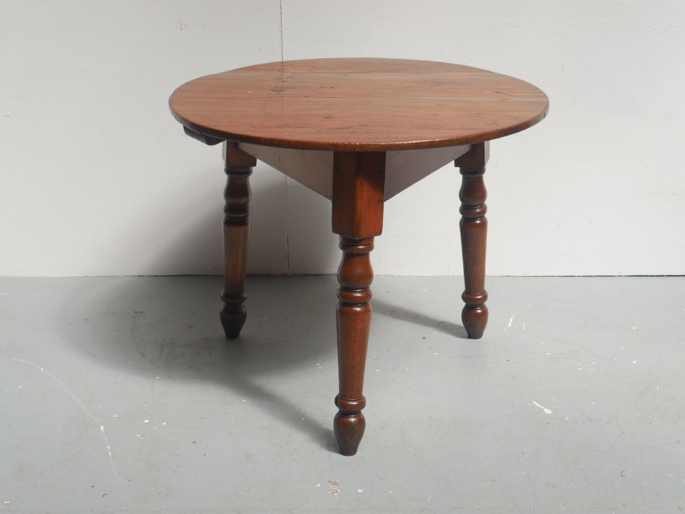 A circular pine cricket table featuring three turned legs joined by a deep triangular apron in a warm brown timber finish. View VII