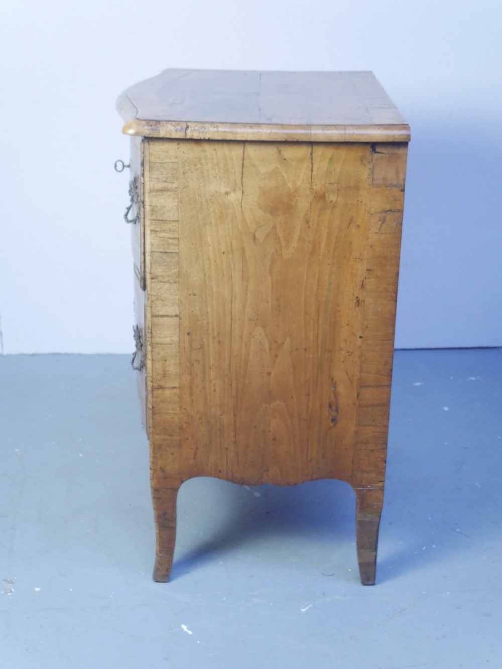 An 18th-century Swedish wooden commode featuring two bow-fronted drawers, ornamental brass handles, escutcheons, and curved lower legs. View VI