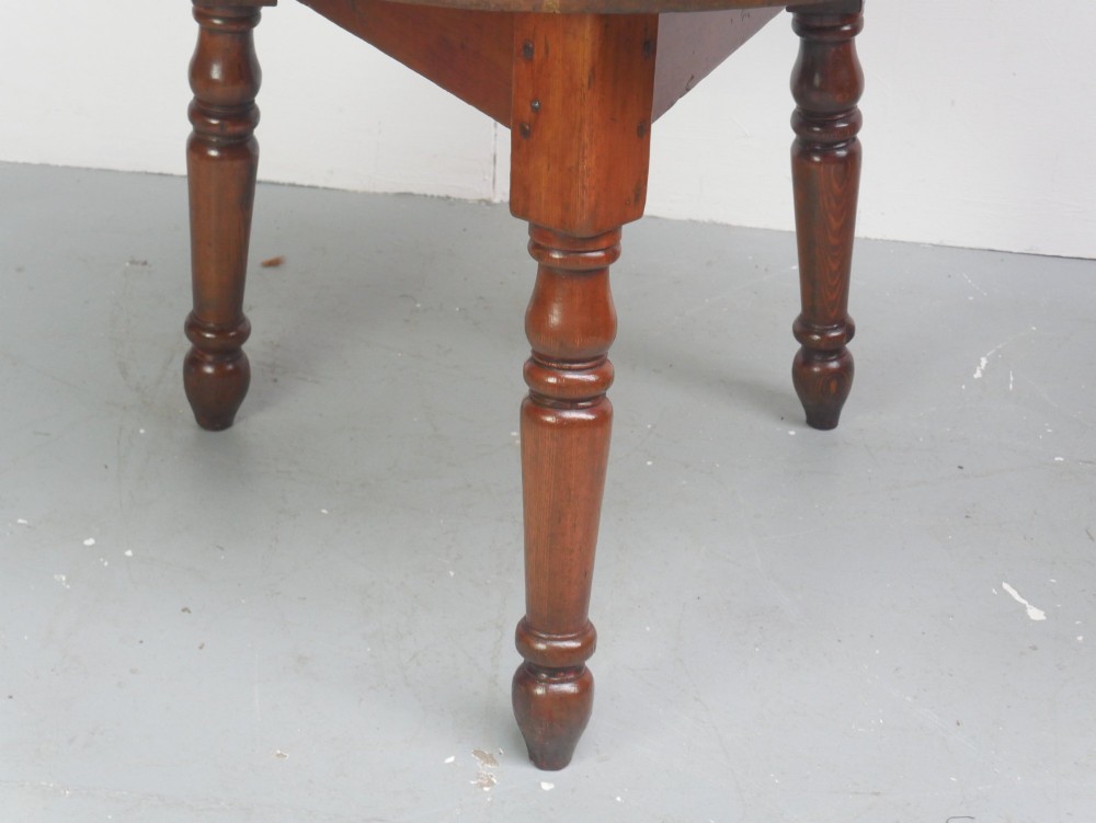 A circular pine cricket table featuring three turned legs joined by a deep triangular apron in a warm brown timber finish. View VIII