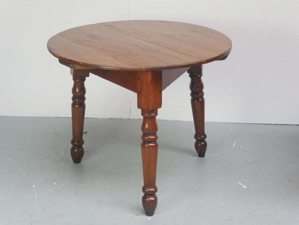 A circular pine cricket table featuring three turned legs joined by a deep triangular apron in a warm brown timber finish.