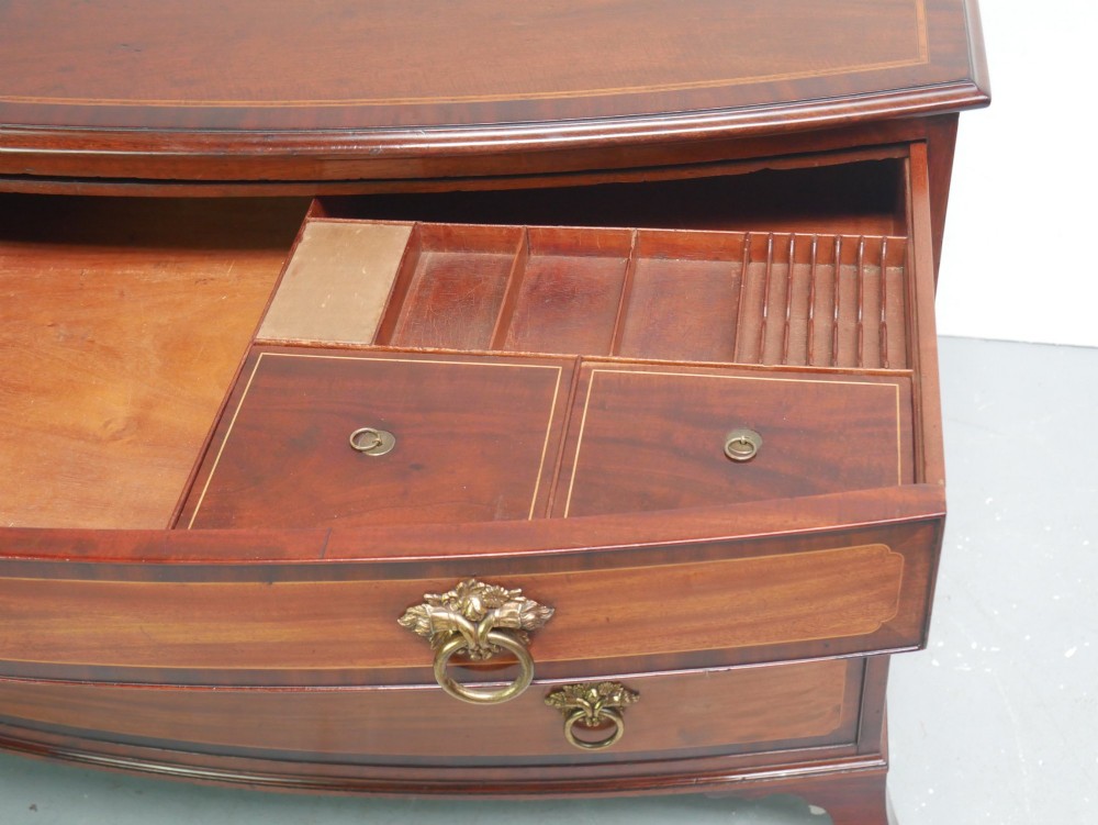 A Georgian flame mahogany bowfront chest of drawers featuring four graduating drawers with brass ring handles and bracket feet. View VIII
