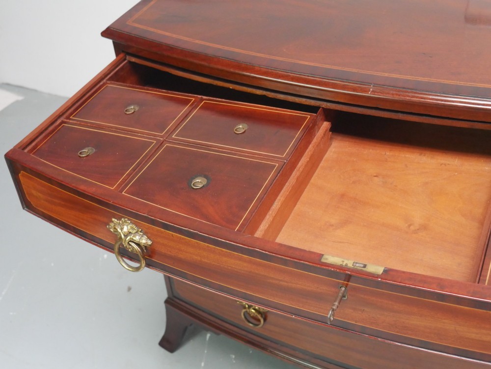 A Georgian flame mahogany bowfront chest of drawers featuring four graduating drawers with brass ring handles and bracket feet. View IX