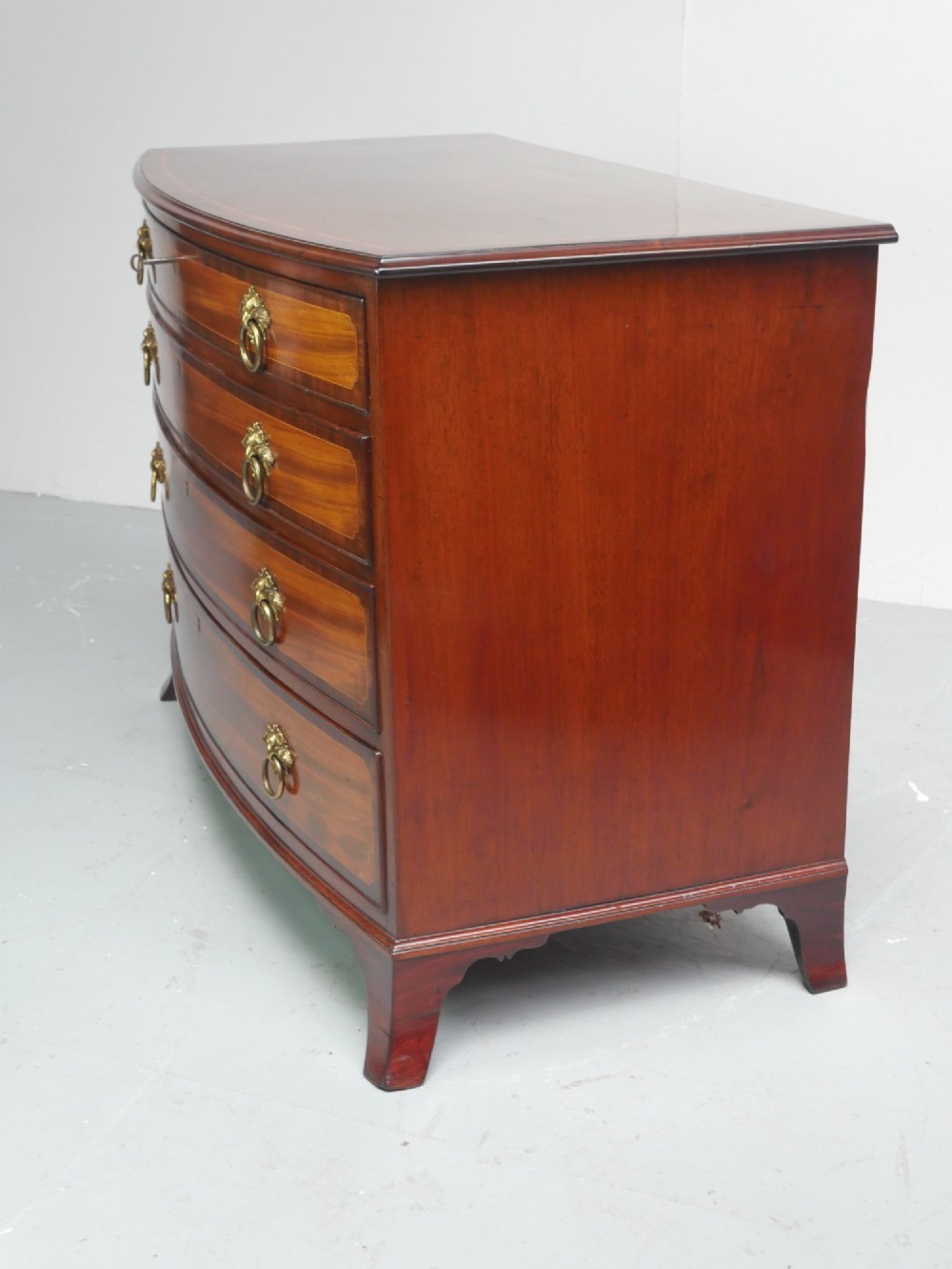 A Georgian flame mahogany bowfront chest of drawers featuring four graduating drawers with brass ring handles and bracket feet. View XI