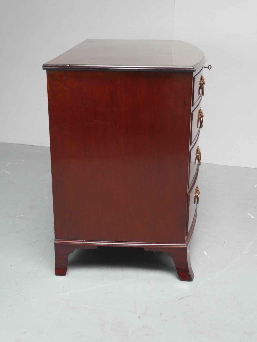 A Georgian flame mahogany bowfront chest of drawers featuring four graduating drawers with brass ring handles and bracket feet. View XIII