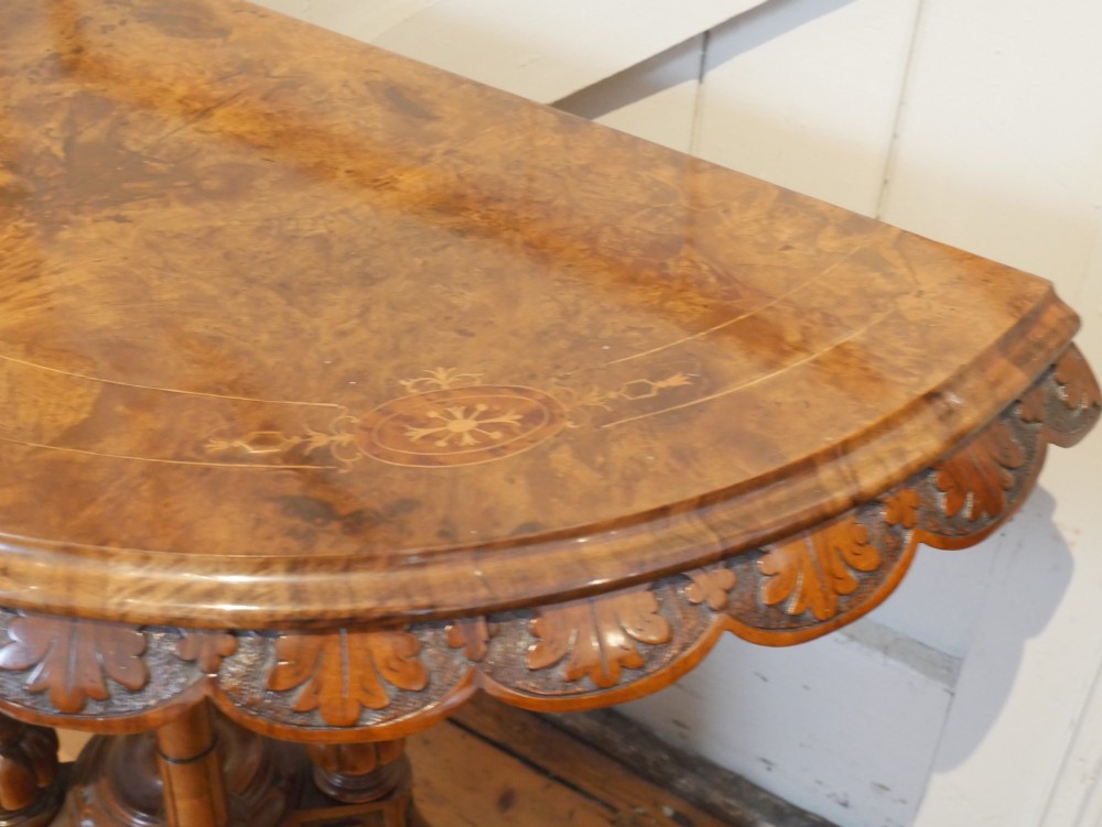 A 19th-century Irish walnut fold-over games table with a scalloped carved apron, turned twin pedestal supports, and carved splayed legs on white castors. View II