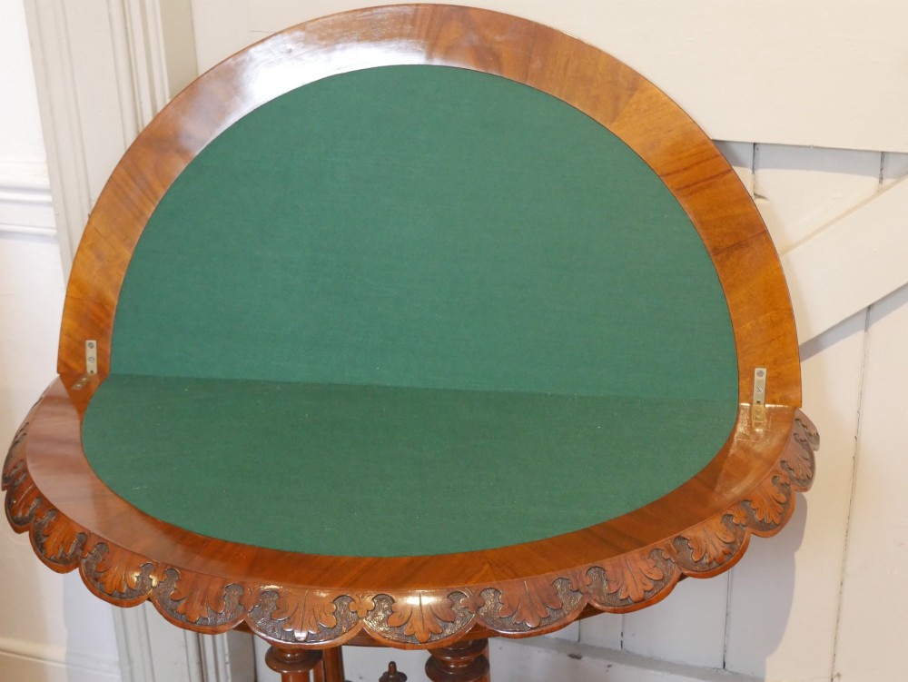 A 19th-century Irish walnut fold-over games table with a scalloped carved apron, turned twin pedestal supports, and carved splayed legs on white castors. View IV