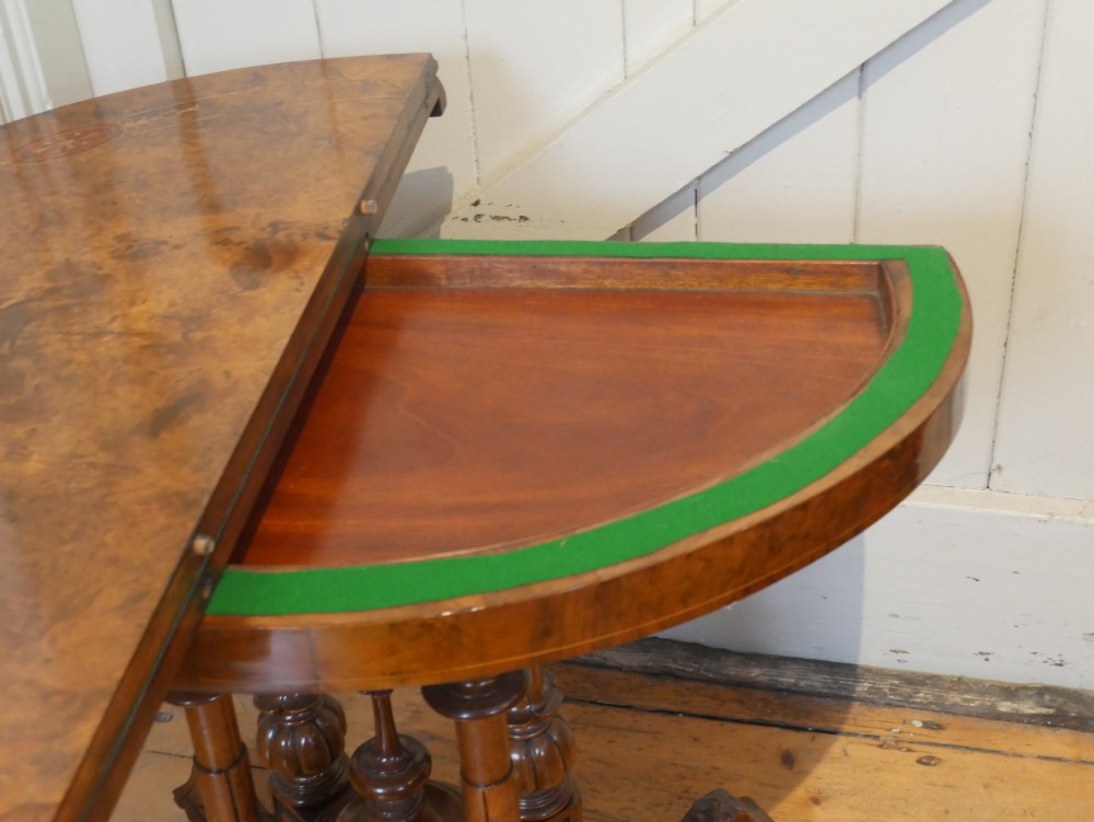 A 19th-century Irish walnut fold-over games table with a scalloped carved apron, turned twin pedestal supports, and carved splayed legs on white castors. View V