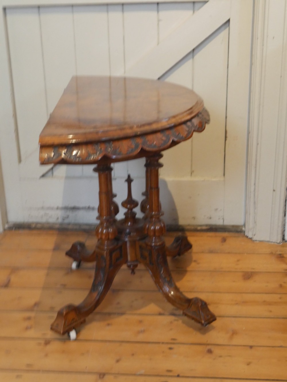 A 19th-century Irish walnut fold-over games table with a scalloped carved apron, turned twin pedestal supports, and carved splayed legs on white castors. View VII