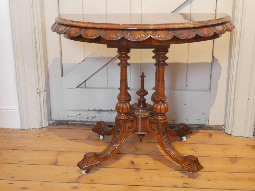 A 19th-century Irish walnut fold-over games table with a scalloped carved apron, turned twin pedestal supports, and carved splayed legs on white castors. View IX
