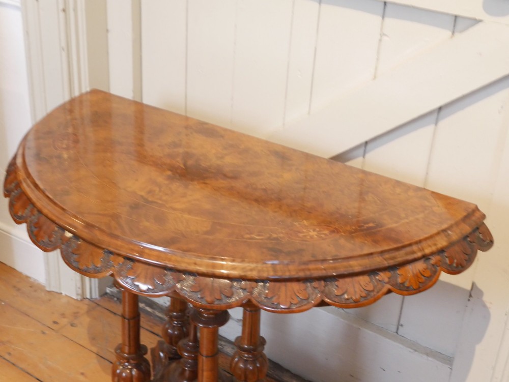 A 19th-century Irish walnut fold-over games table with a scalloped carved apron, turned twin pedestal supports, and carved splayed legs on white castors. View X